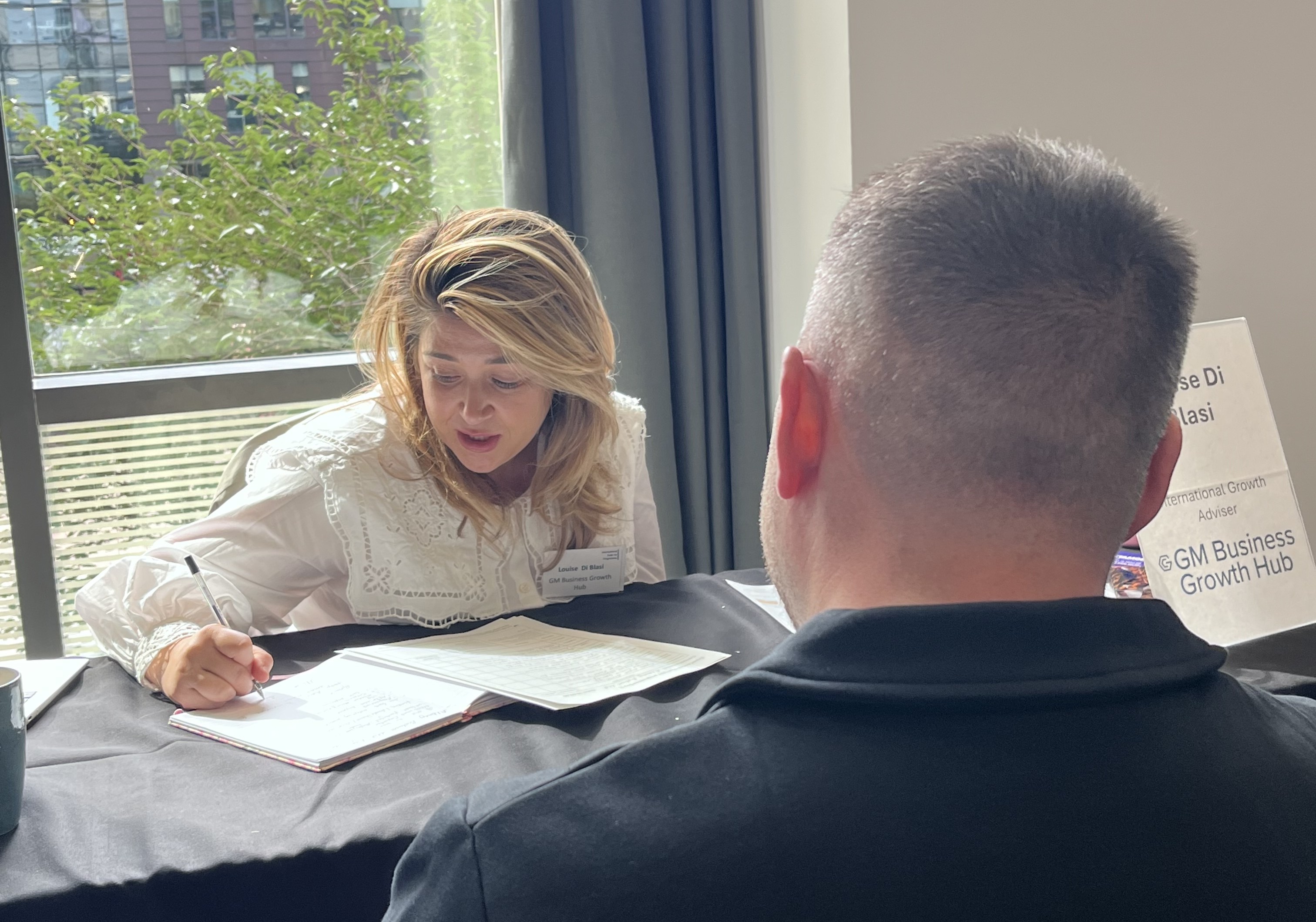 Woman writing down notes whilst conversing with a man.